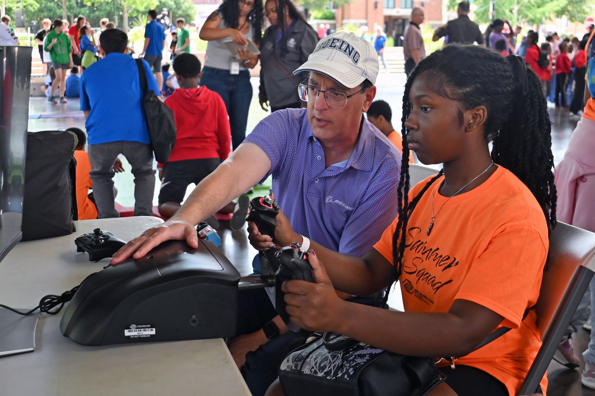 Two people at a table using a braille display in a busy public outdoor event
