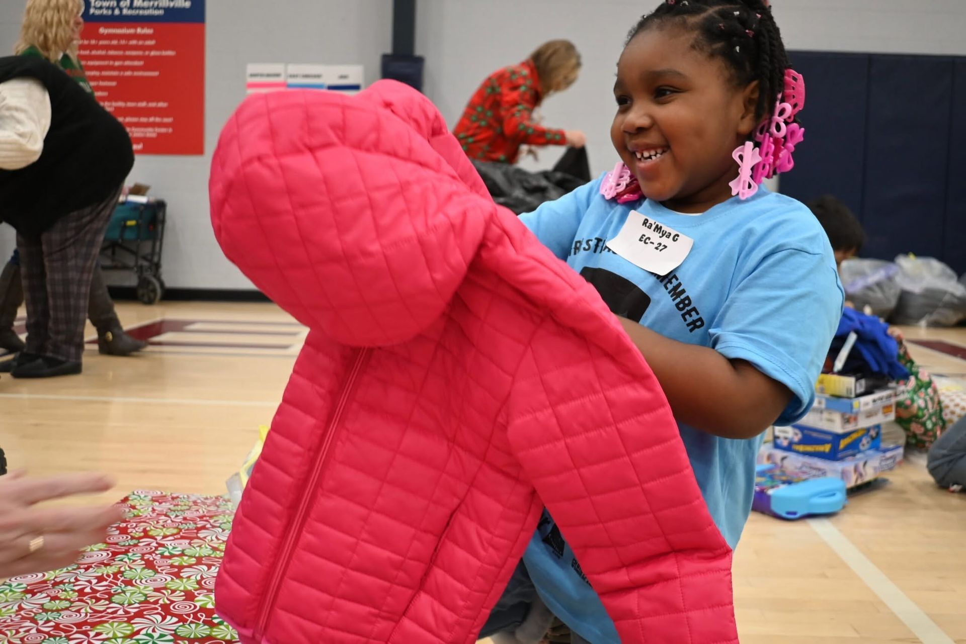 Child holding a bright pink hooded jacket at a clothing donation event in a gymnasium