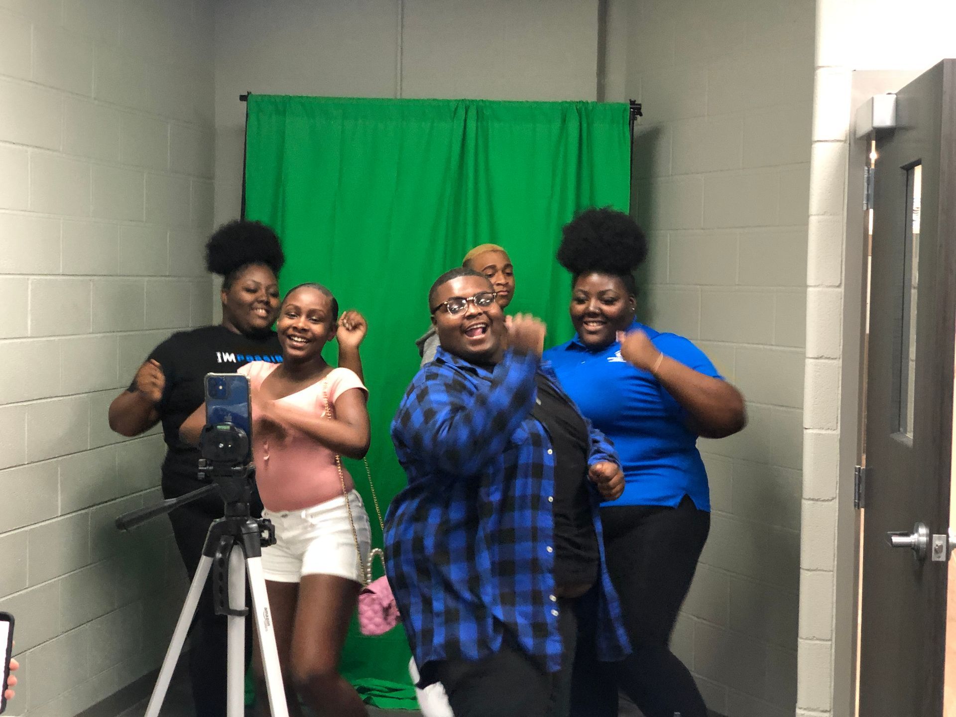 Four smiling people posing for a selfie in front of a green backdrop in a hallway
