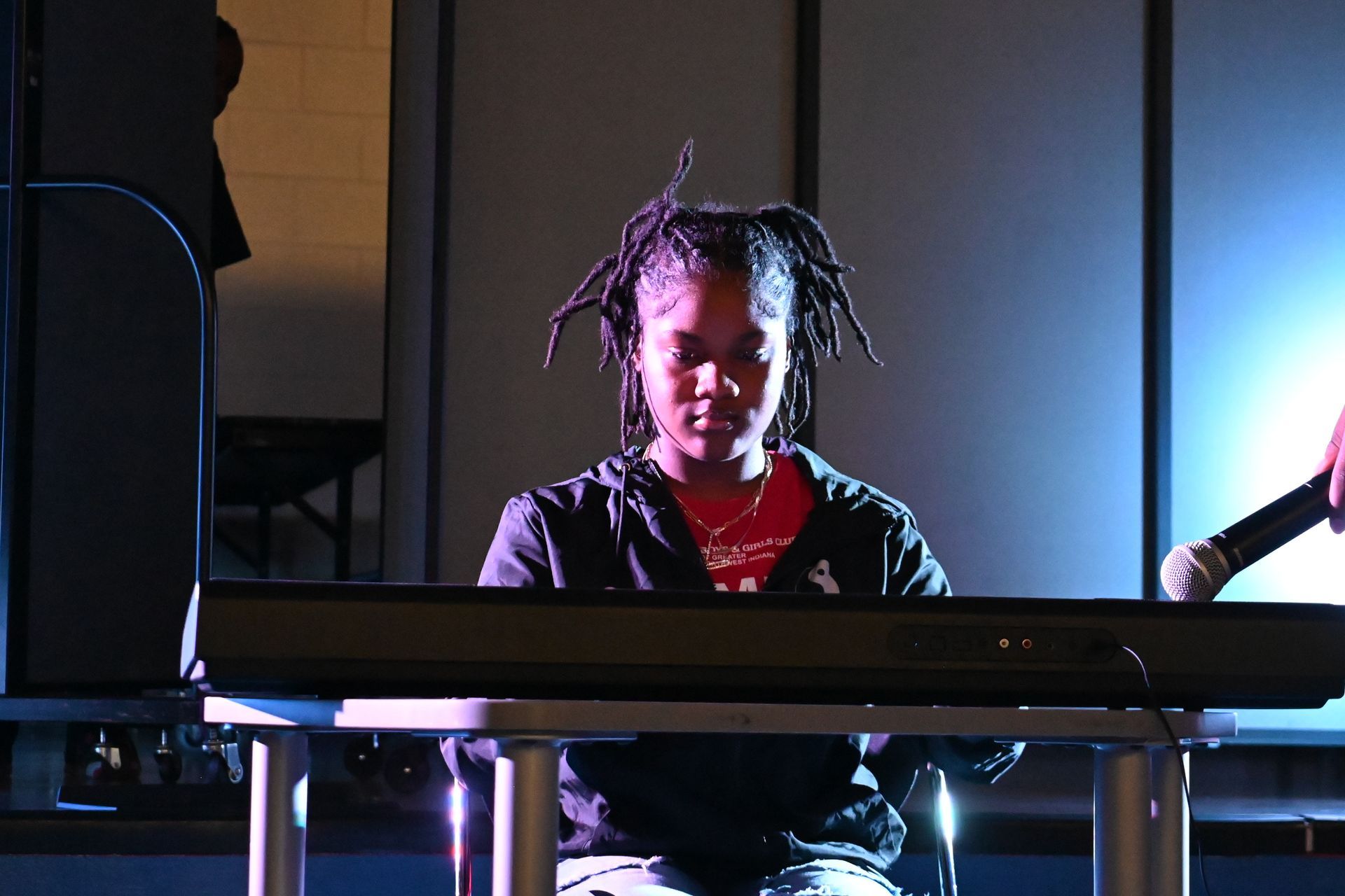 Person seated at a keyboard in a dim studio, lit by blue and purple stage lights.