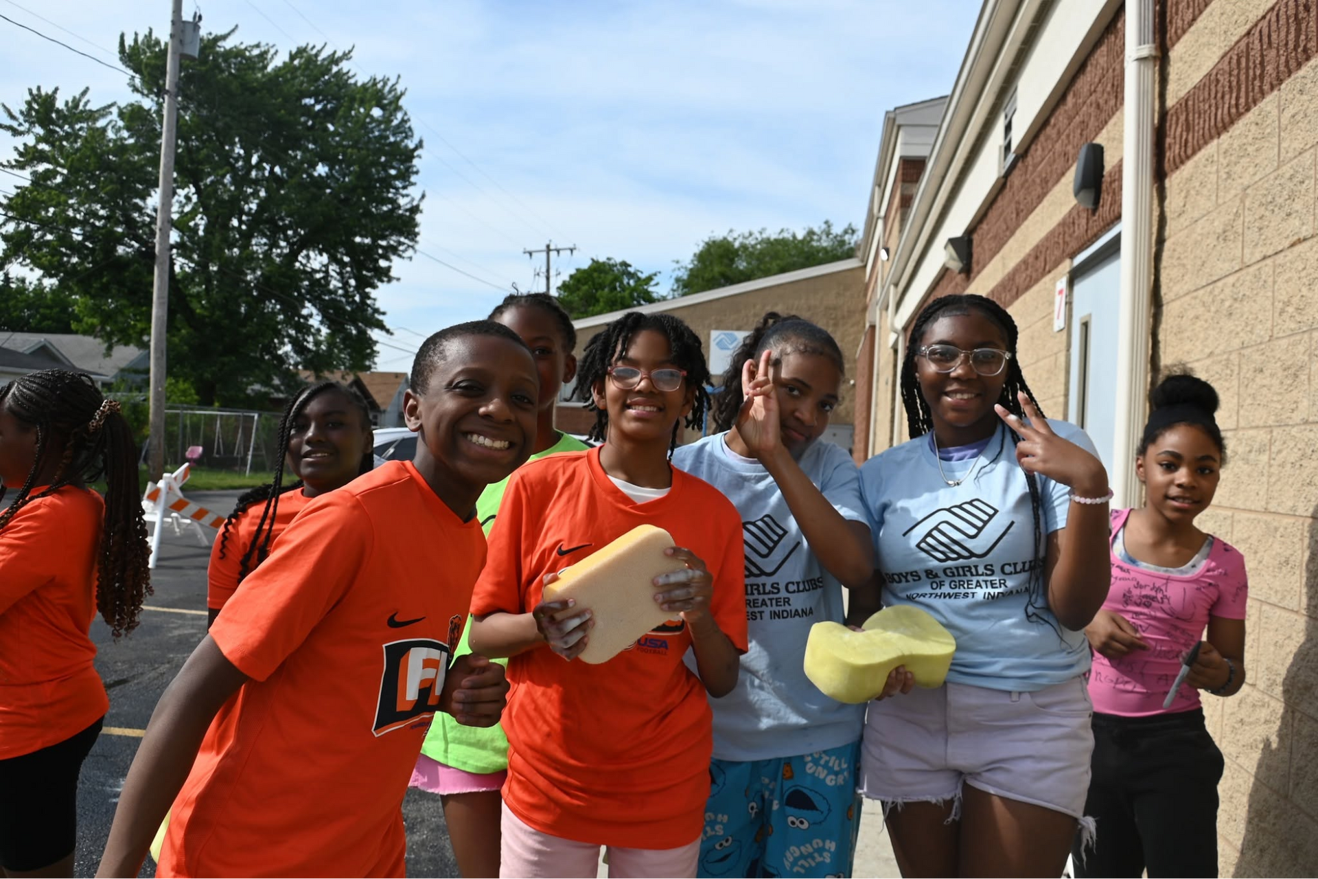 People smiling and holding food containers outside a brick building on a sunny day