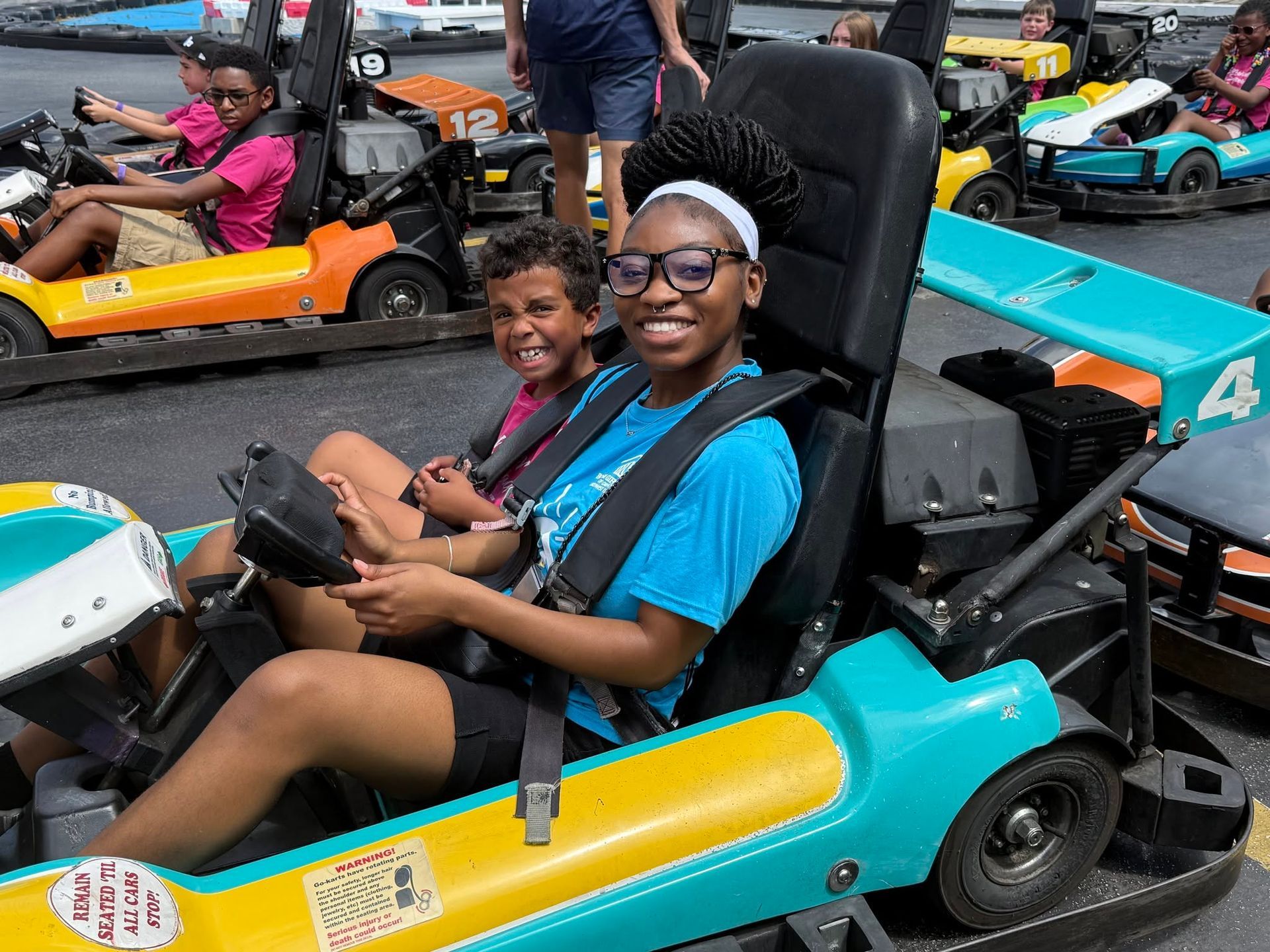 Two people smiling in turquoise and yellow go-karts on a track