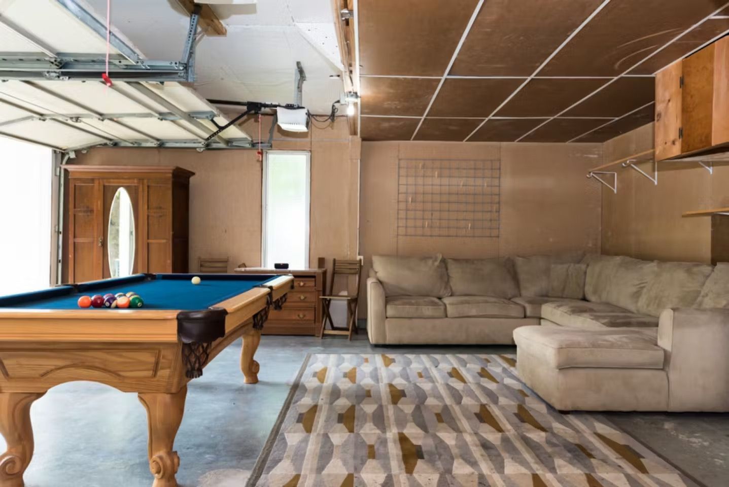 Spacious basement with pool table, sectional sofa, patterned rug, and garage door opener overhead.