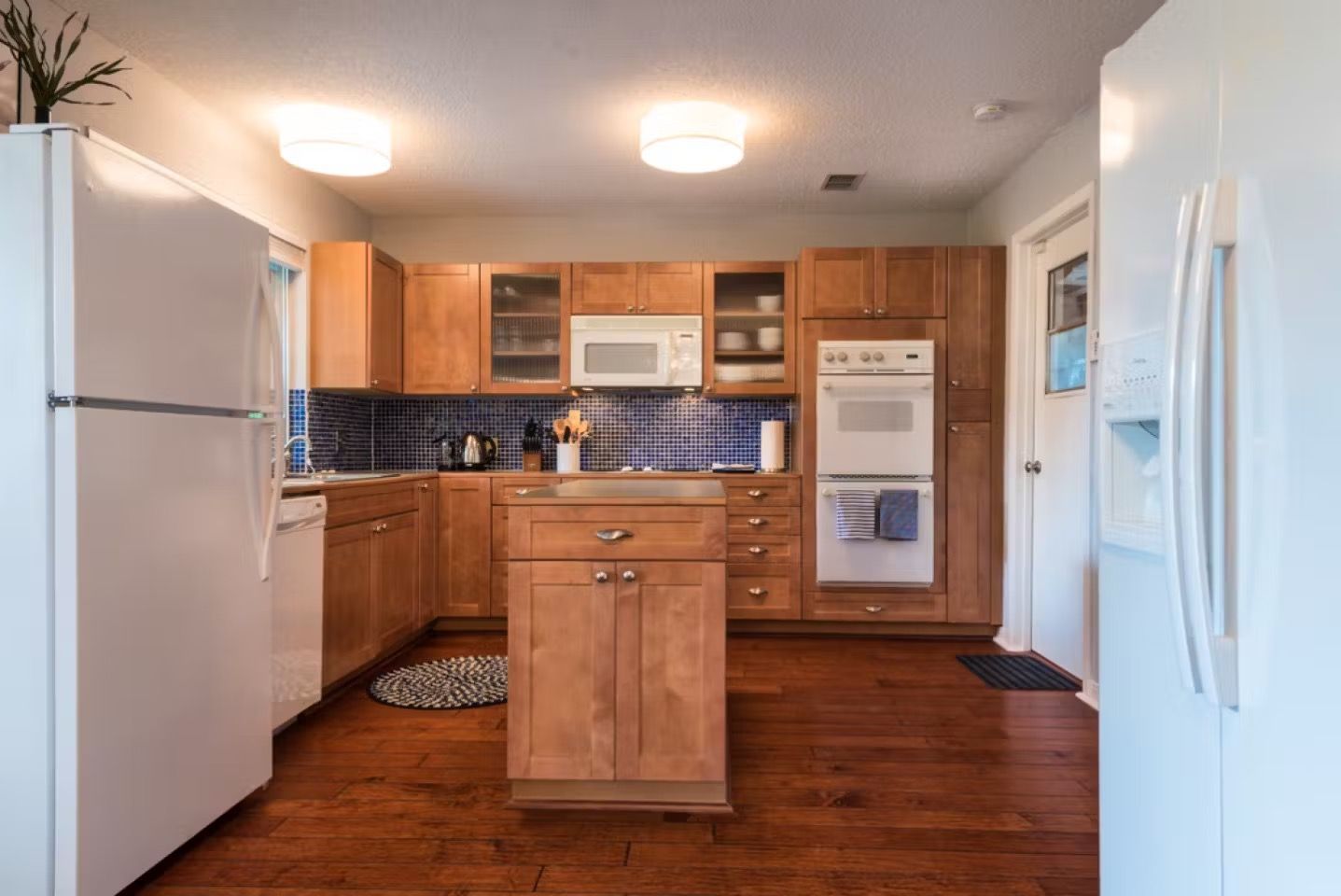 Bright kitchen with white appliances, wood cabinets, blue tile backsplash, and hardwood floors