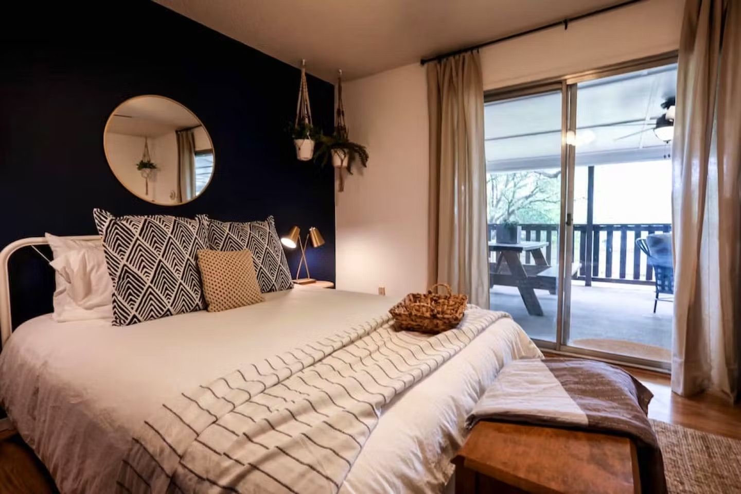 Cozy bedroom with a bed, round mirror, and sliding doors opening to a balcony with outdoor seating