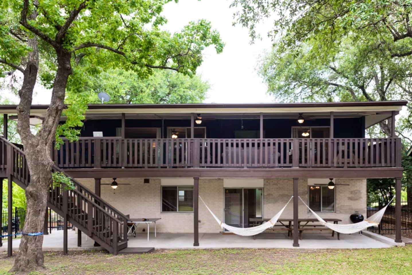 Two-story house with a wooden porch, staircase, and two white hammocks under large trees