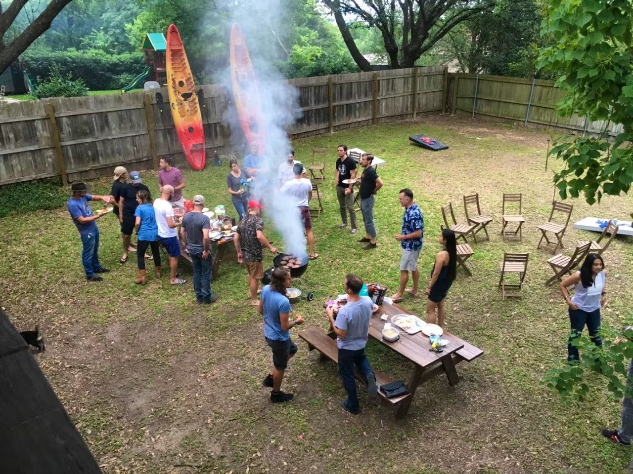 People gathered in a backyard around a smoking rocket launch, with chairs and tables nearby.
