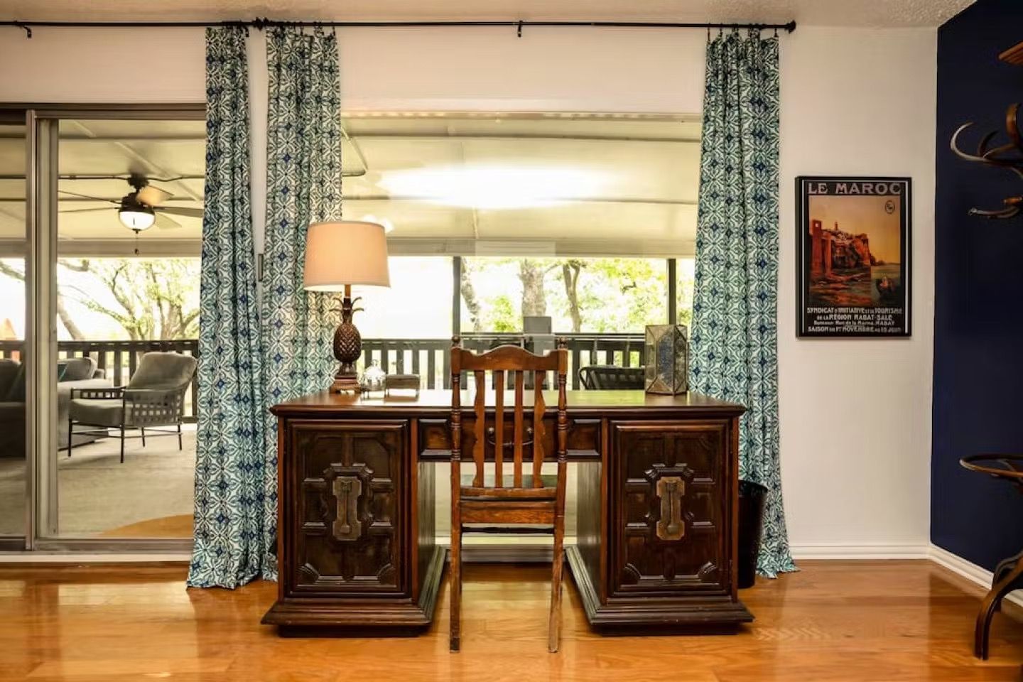 Home office with dark wood desk, lamp, patterned curtains, and sliding glass doors to a patio.
