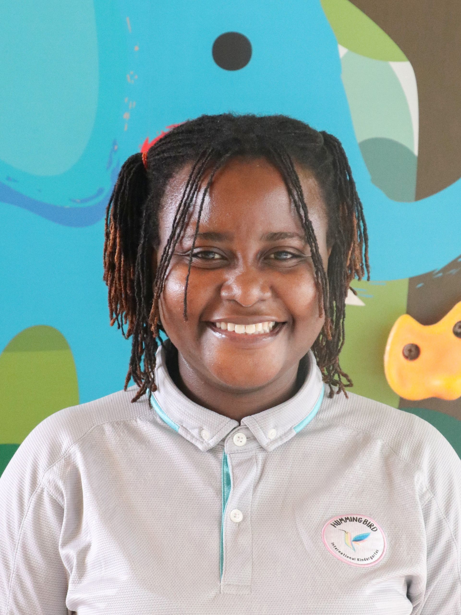 Woman smiling, wearing white shirt, against a backdrop of a colorful mural in a playful setting.