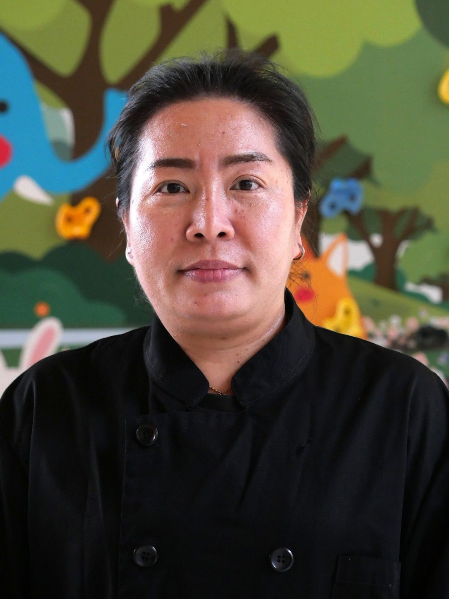Woman in black uniform, smiling slightly, in front of a colorful mural.