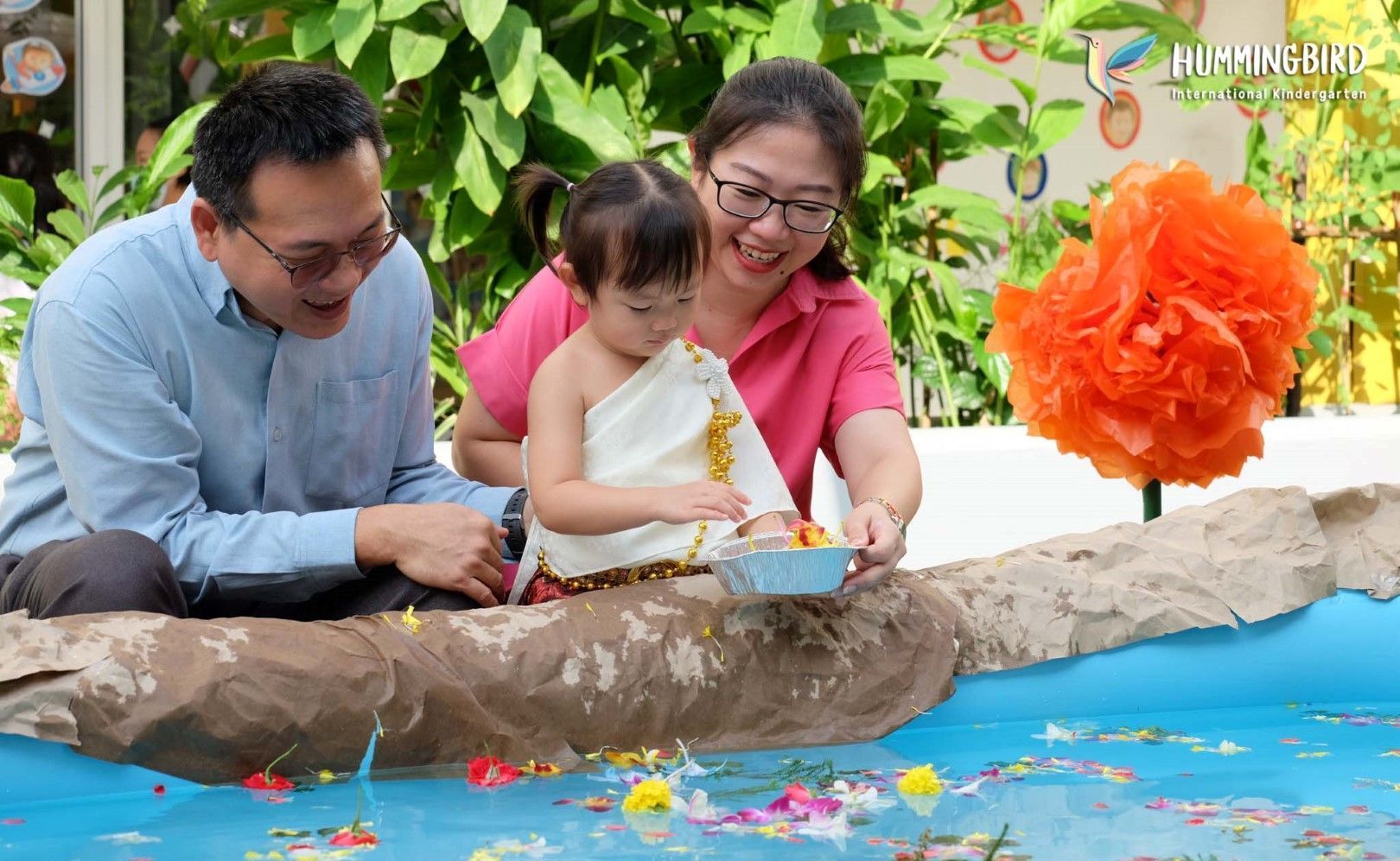 A man and woman are sitting next to a little girl in a pool of water.