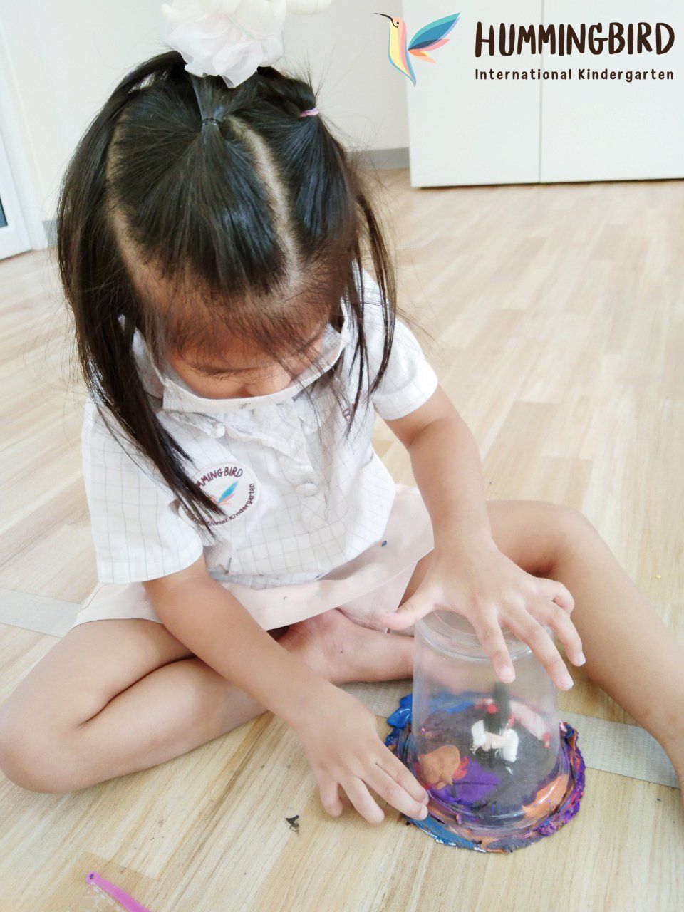 A little girl is sitting on the floor playing with a hummingbird toy