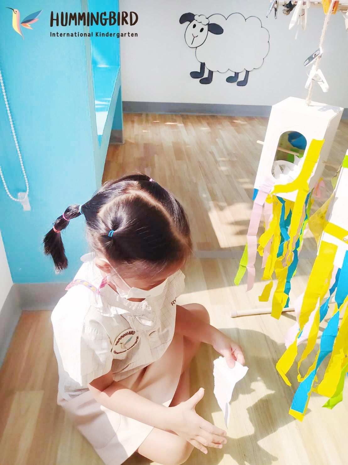A little girl wearing a mask is kneeling on the floor.