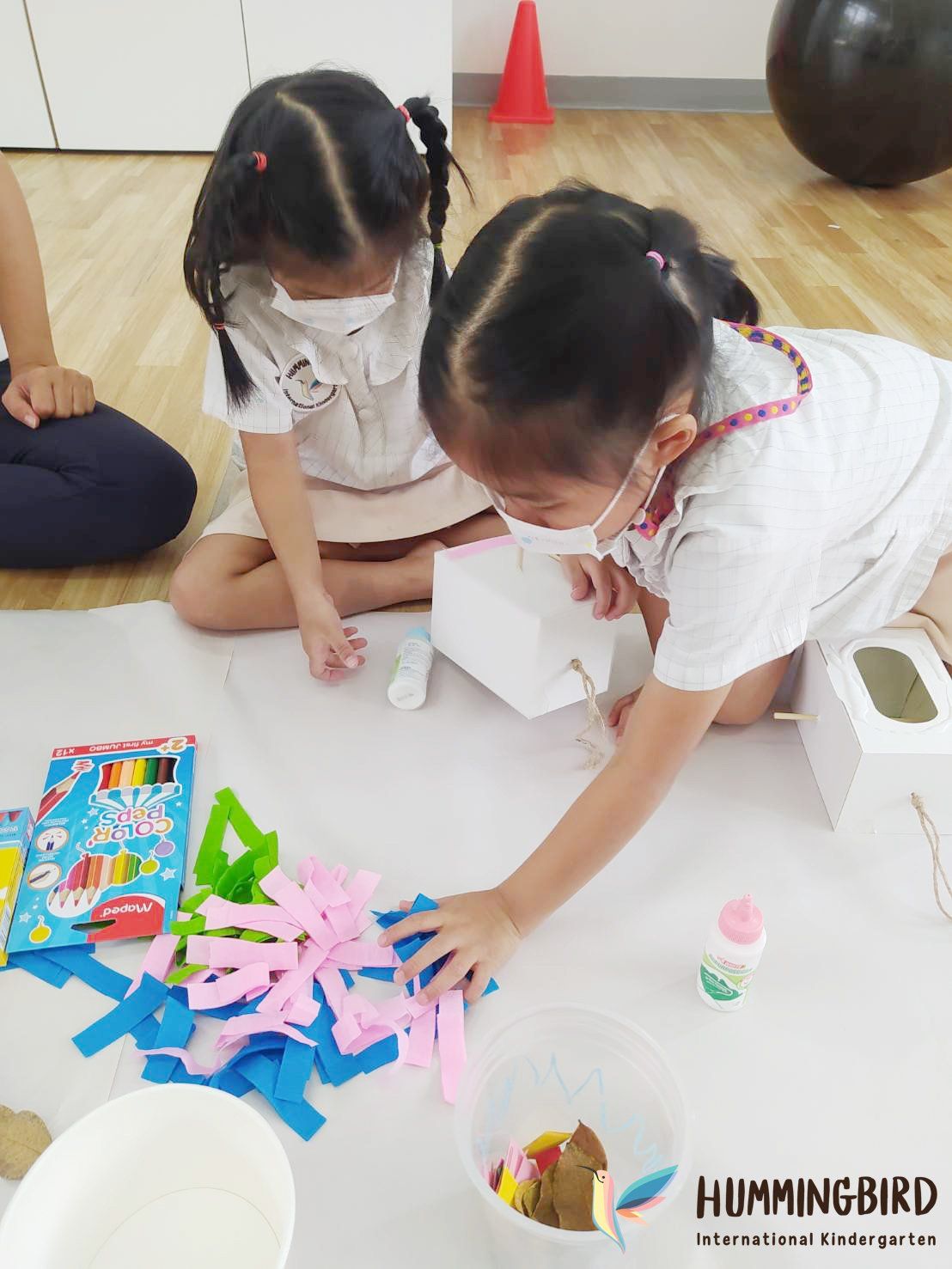 Two little girls are sitting on the floor making crafts.