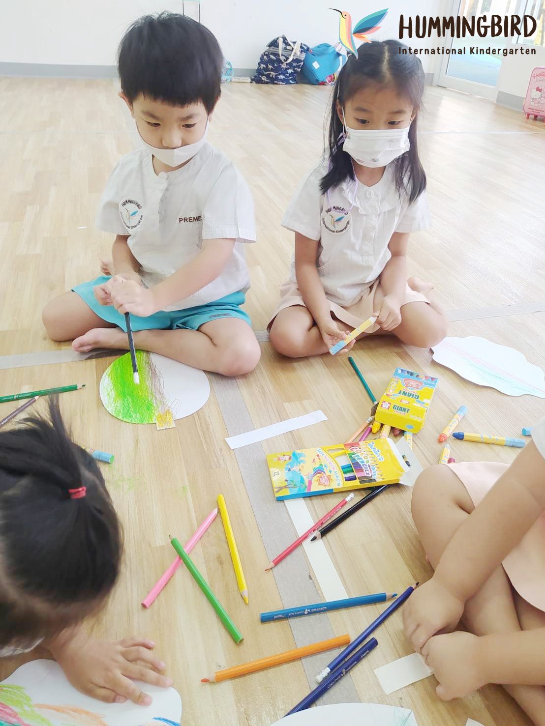 A group of children are sitting on the floor drawing with colored pencils.