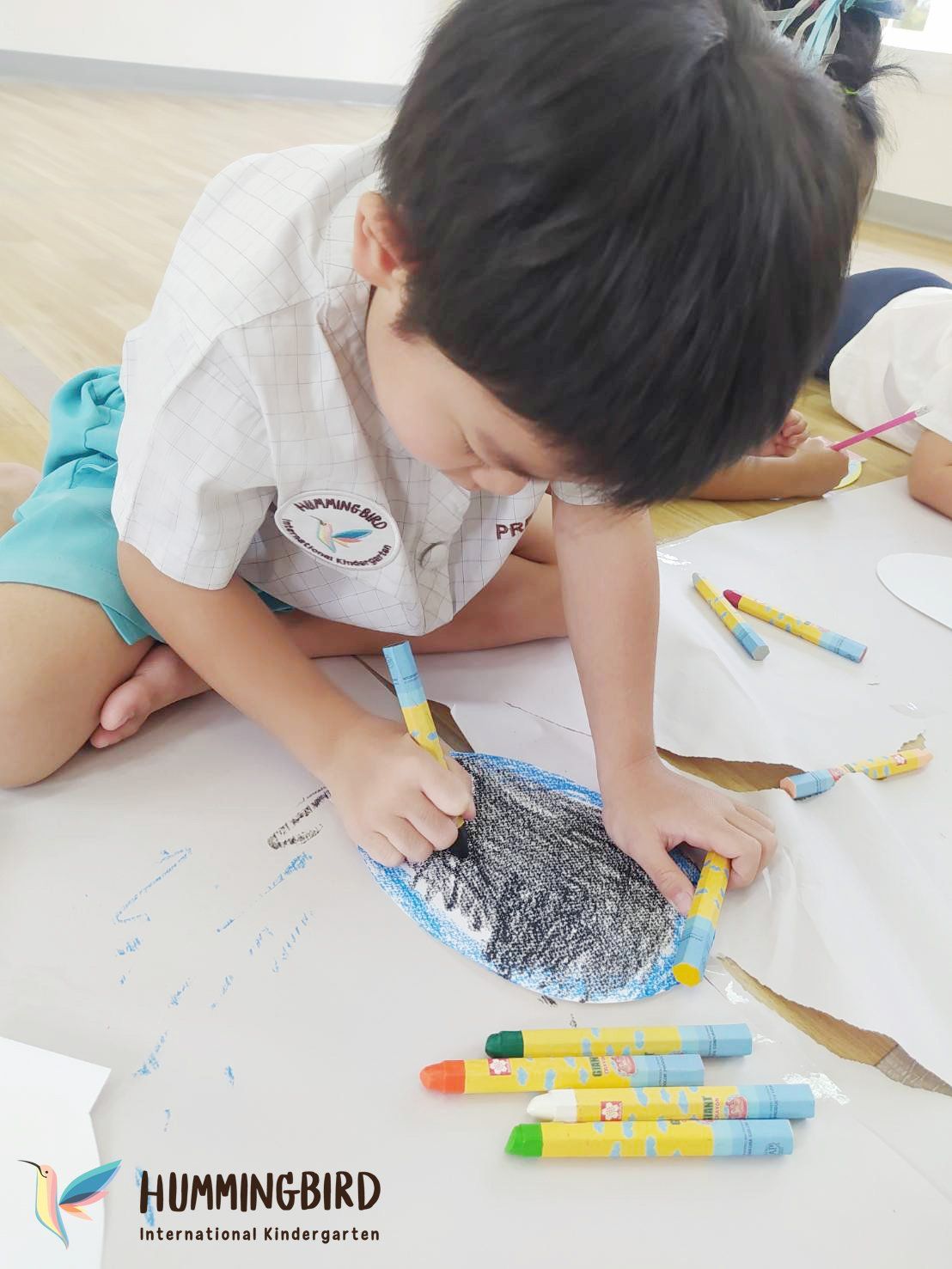 A young boy is sitting on the floor drawing with crayons.
