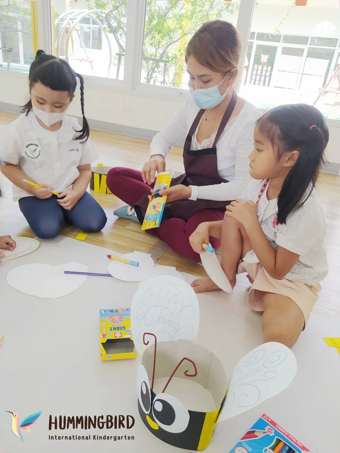 A group of children are sitting on the floor making crafts.