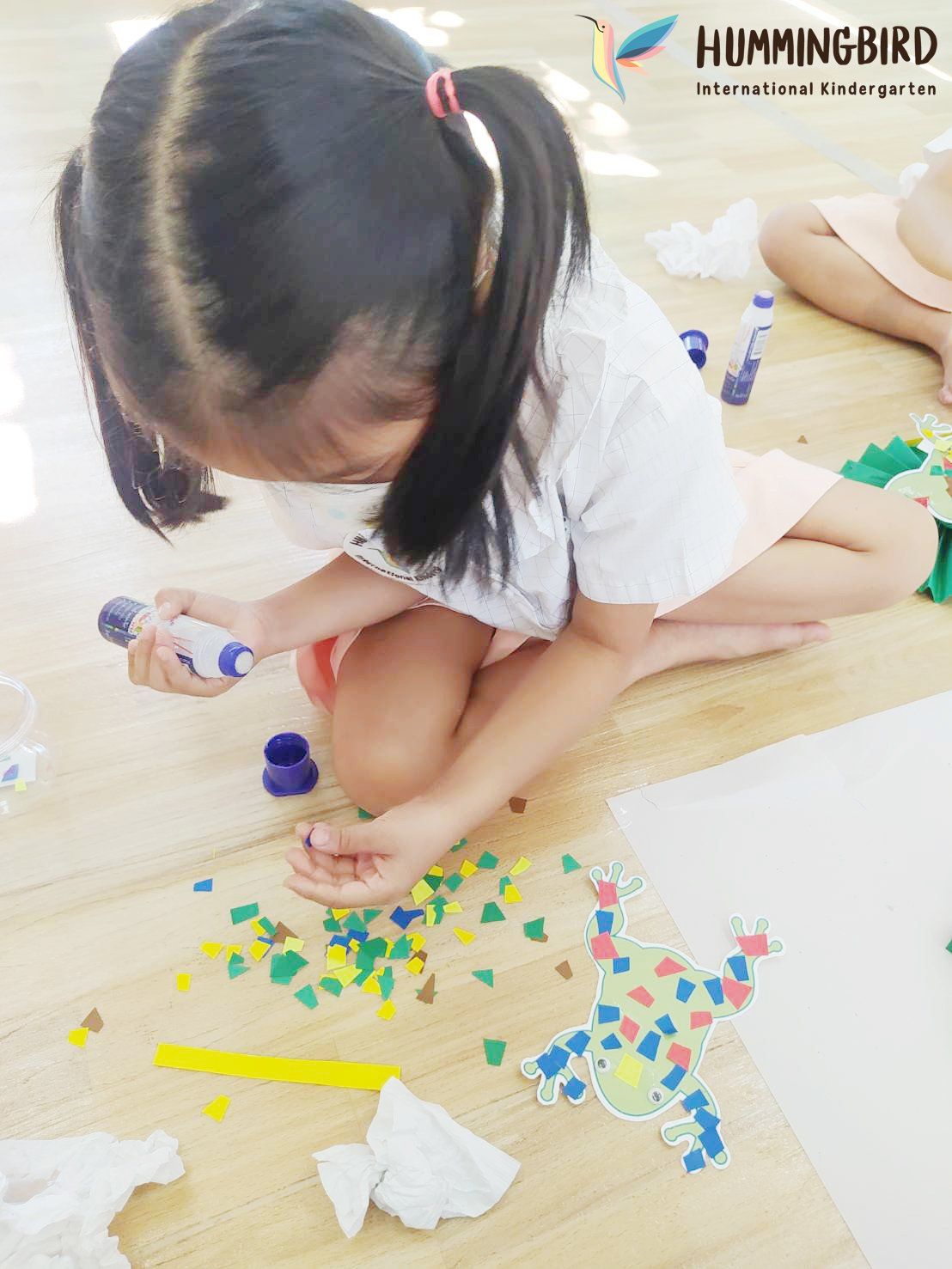 A little girl is sitting on the floor playing with glue.