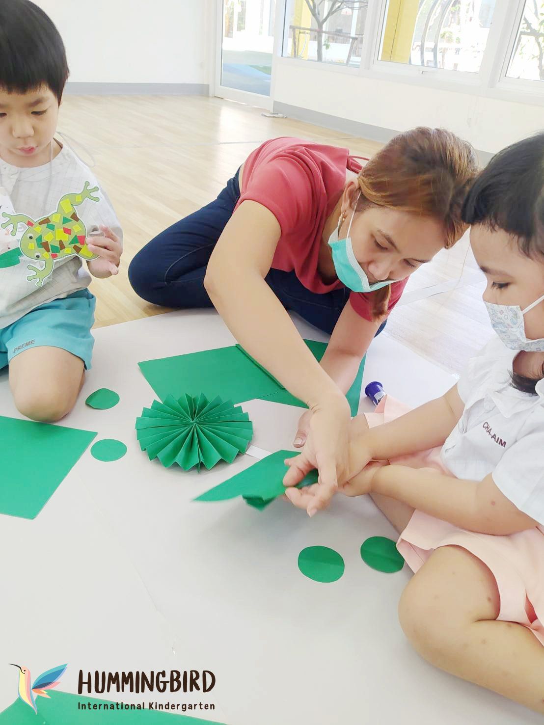 A woman and two children are sitting on the floor making crafts.