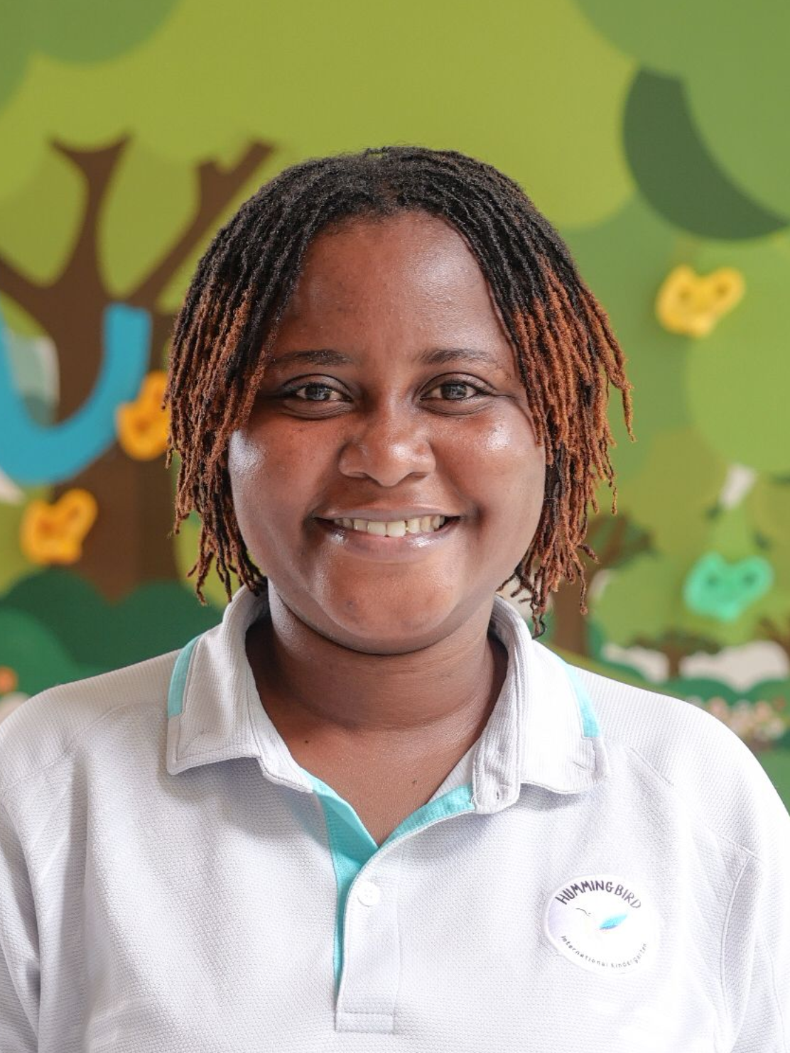 Woman smiling, wearing white shirt, against a backdrop of a colorful mural in a playful setting.