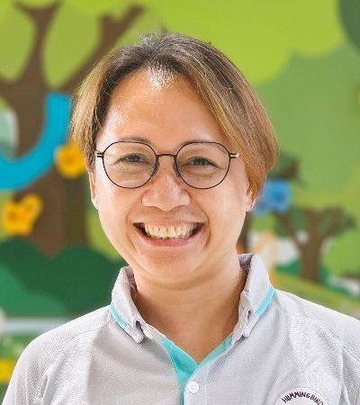 A woman wearing glasses and a gray shirt is smiling.