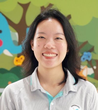 A woman is smiling for the camera in front of a painting of trees and flowers.