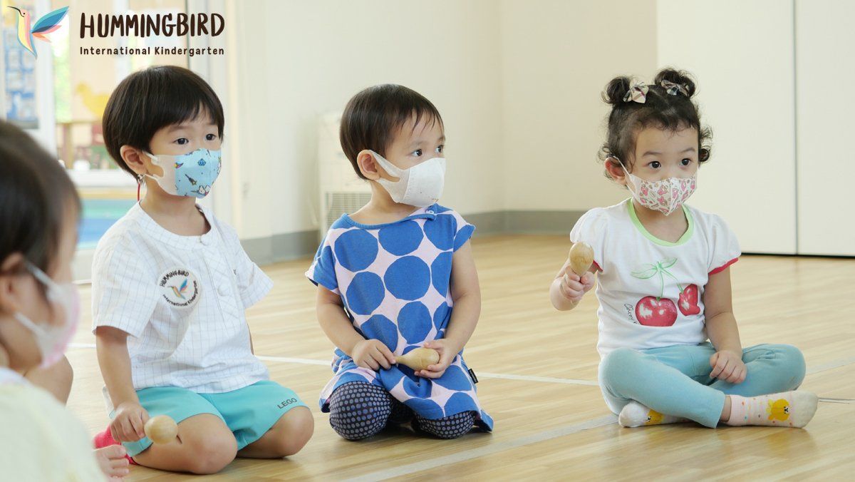 Three children wearing face masks are sitting on the floor in a room.
