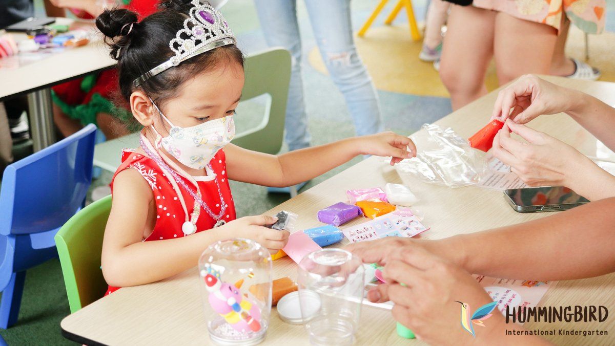 A little girl wearing a tiara and a mask is sitting at a table.