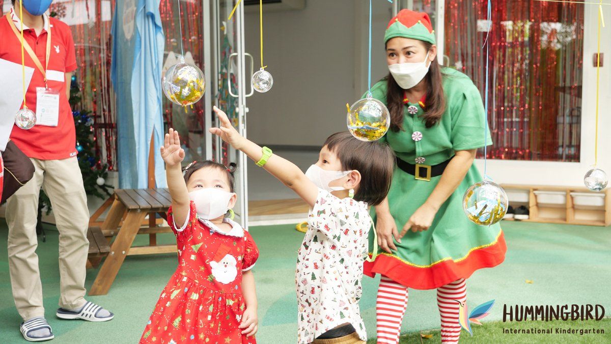A group of children wearing face masks and elf costumes are playing with christmas decorations.