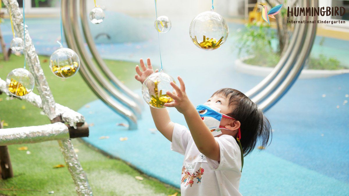 A little girl wearing a mask is playing with a water fountain.