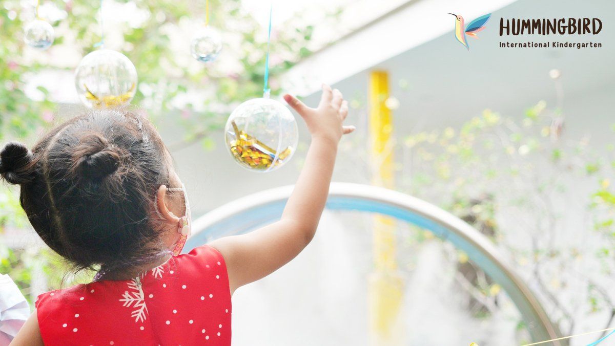 A little girl in a red dress is blowing soap bubbles.
