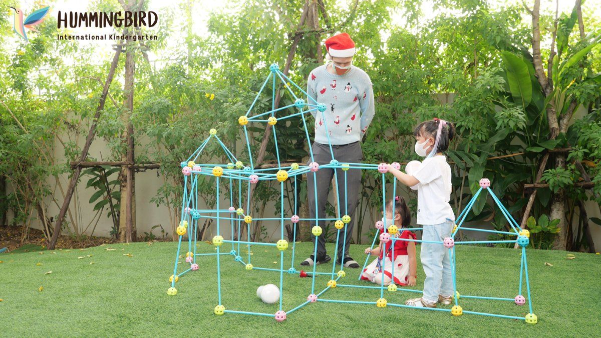 A man and a little girl are playing with a castle made of plastic tubes.