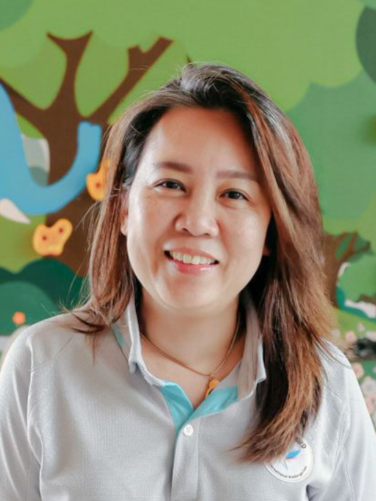 Woman smiling, wearing a light blue collared shirt, in front of a tree mural.