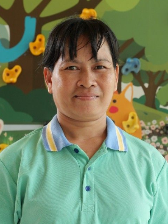 Portrait of a person in a mint-green polo shirt, standing before a colorful classroom mural.