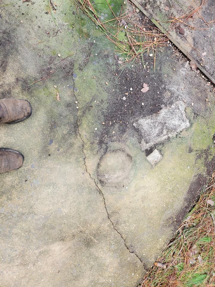 Overhead shot of cracked concrete with circular and rectangular impressions; shoes at left.