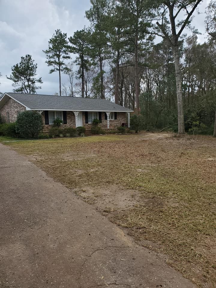 Ranch-style house with dark roof and brick facade, surrounded by trees and a brown lawn, overcast sky.