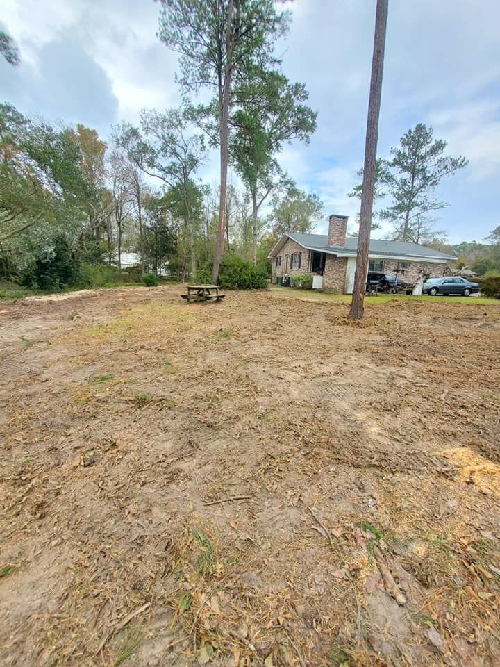 Dirt yard with a house and trees in the background, picnic table in the middle.