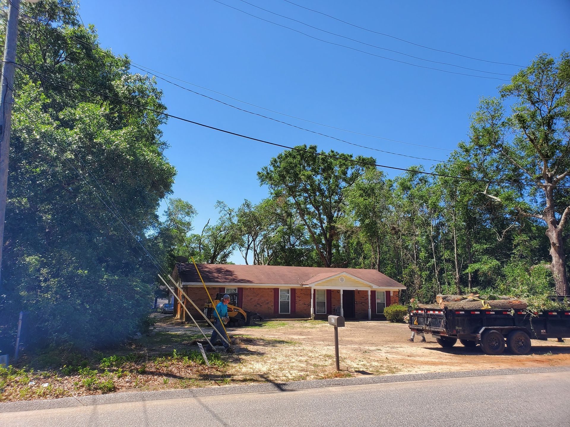 A brick house under a blue sky, with trees surrounding it and a trailer parked nearby.
