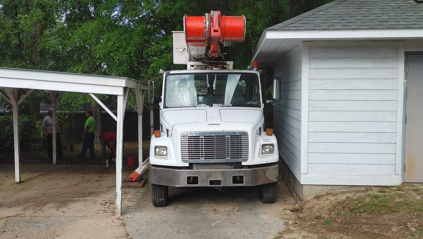 White utility truck with orange lift boom parked near white building and a wooden shelter.