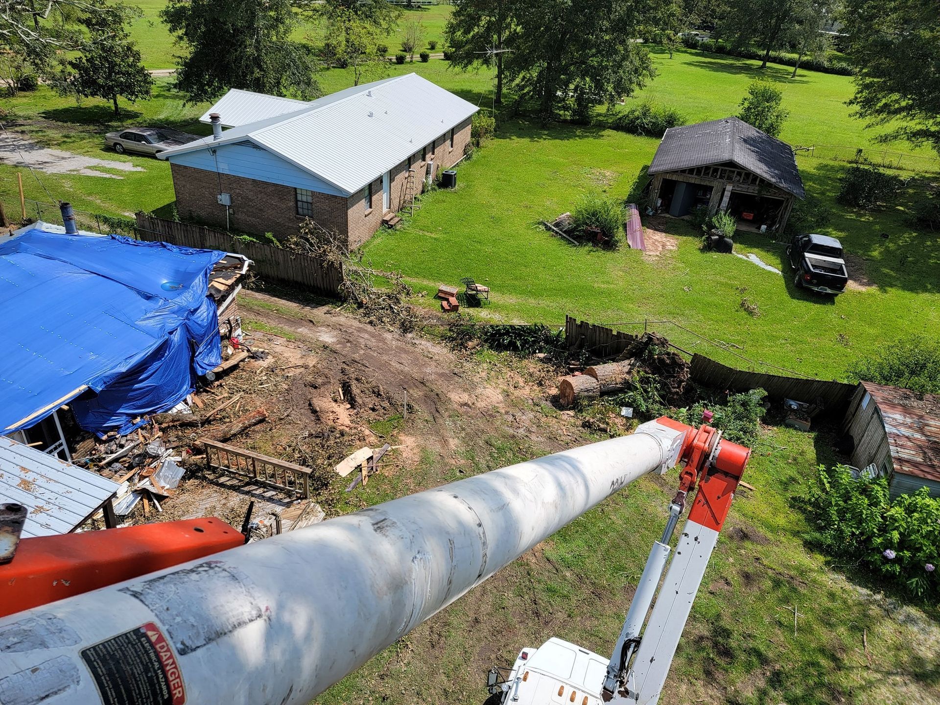 Aerial view of a damaged property with a blue tarp over a structure; an aerial lift in view.