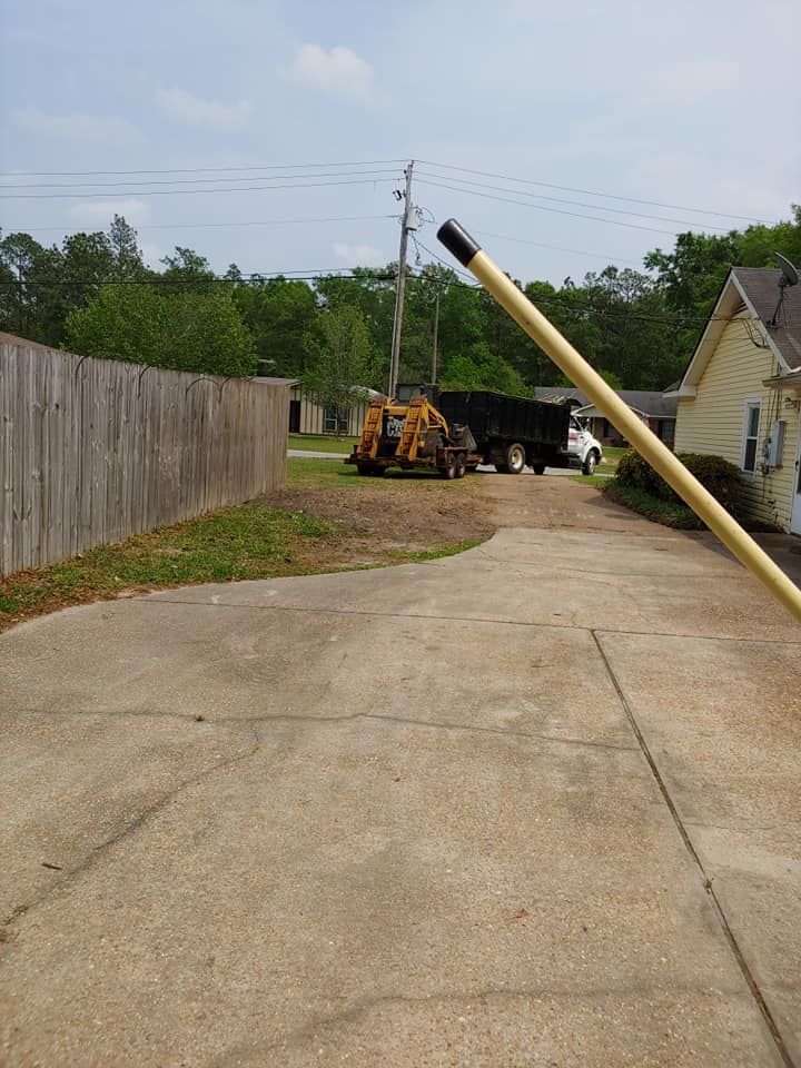 A long, yellow pole angled across a concrete driveway with a truck and equipment in the background.