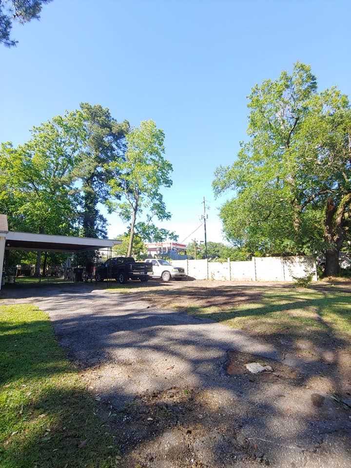 Driveway with parked vehicles; trees and clear sky in the background.