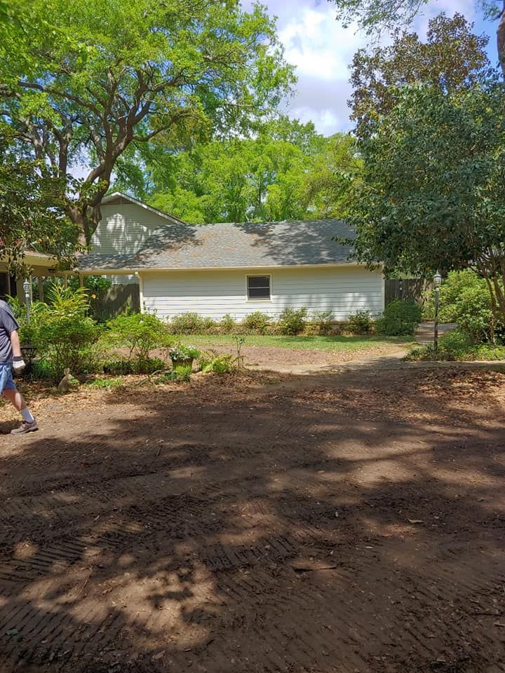 Dirt path leading to a white building with a small window, surrounded by trees. Cloudy sky.