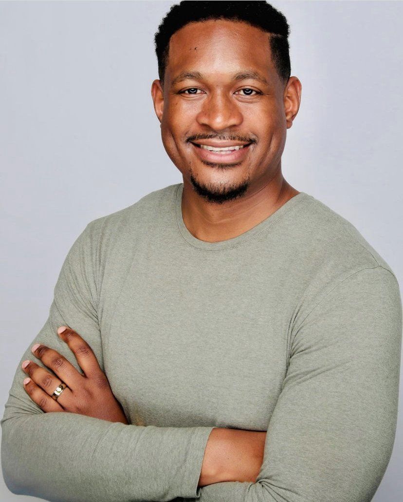 Smiling person wearing a light green long-sleeved shirt with arms crossed, set against a plain light gray background.