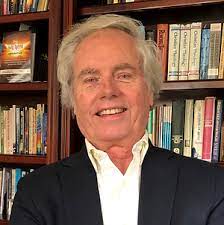 A person smiling in front of a bookshelf filled with various books.