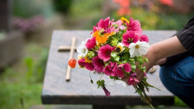 Persona che depone fiori dai colori vivaci su una tomba, con una croce visibile sullo sfondo.