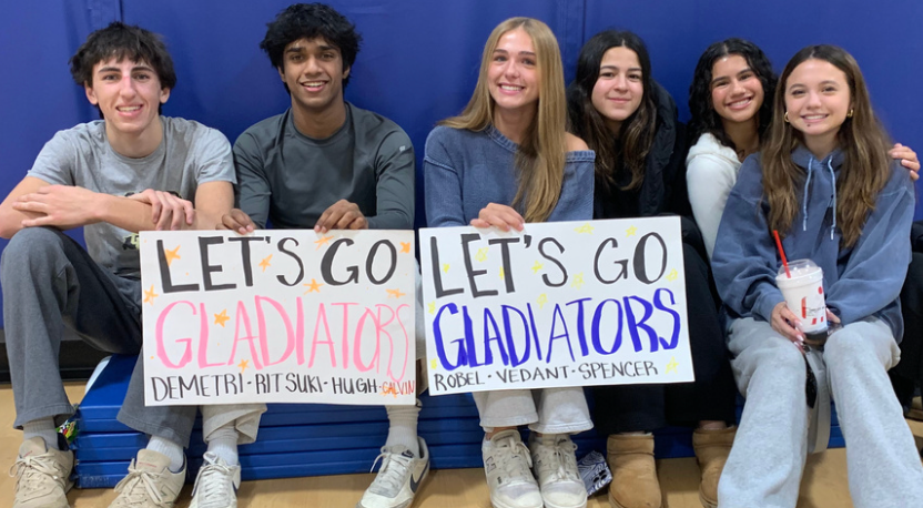 Six smiling students holding “LET’S GO GLADIATORS” signs in bleachers