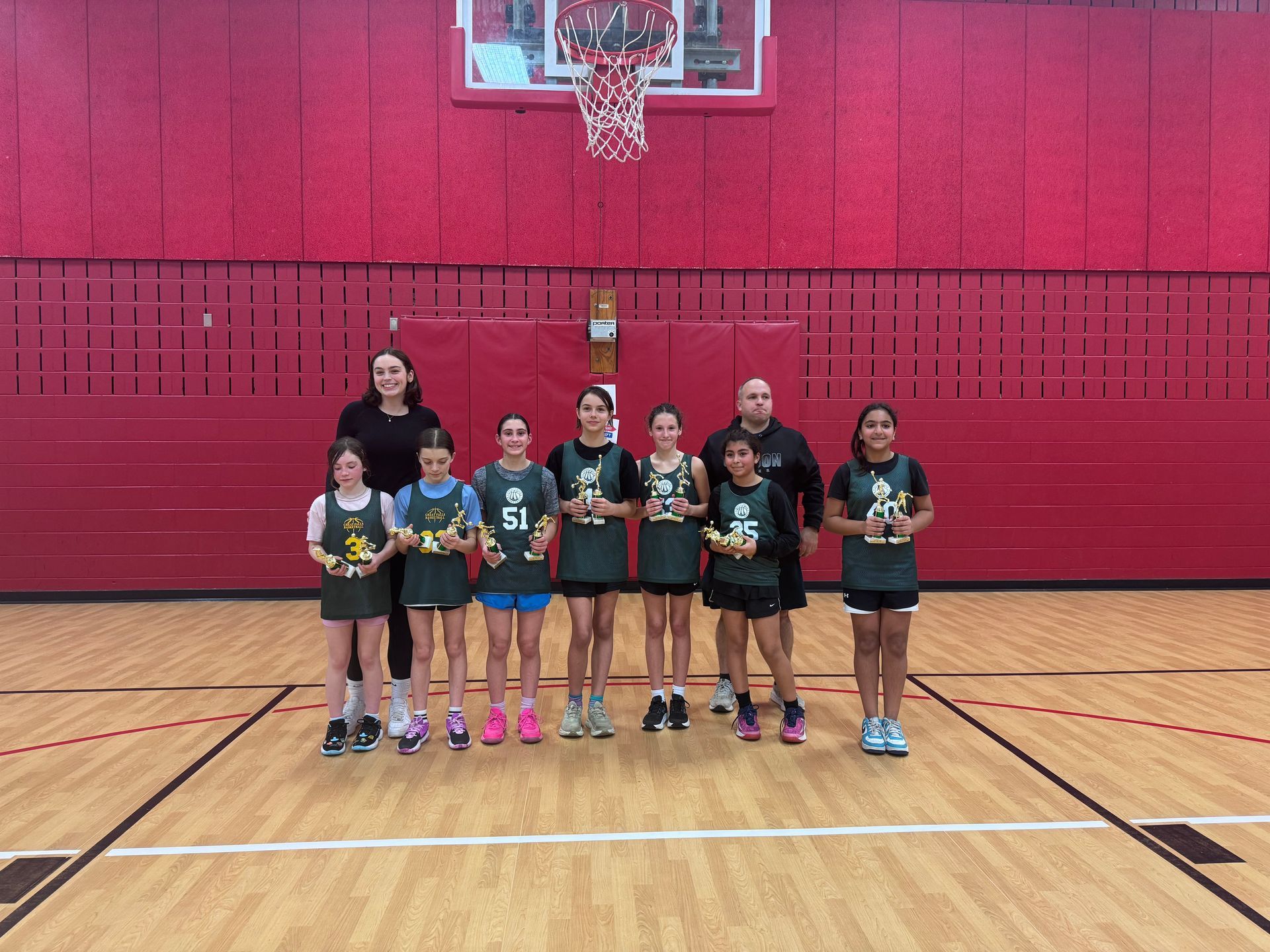 Youth basketball team posing on a gym court in front of a red wall and hoop