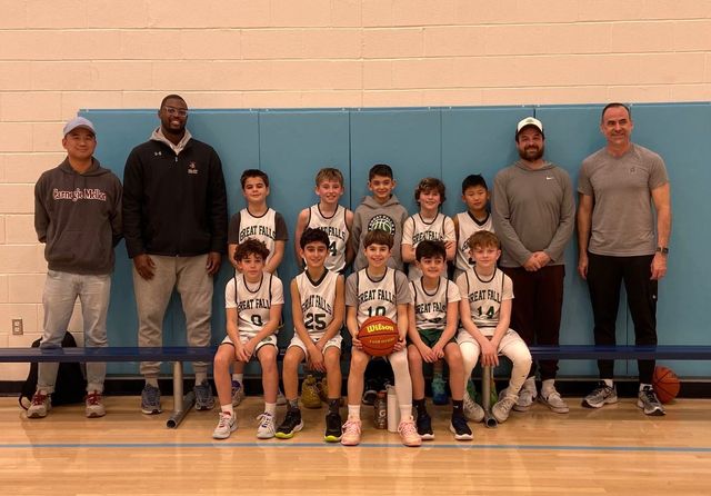Youth basketball team and coaches posing for a group photo in a gym, with players holding a basketball.