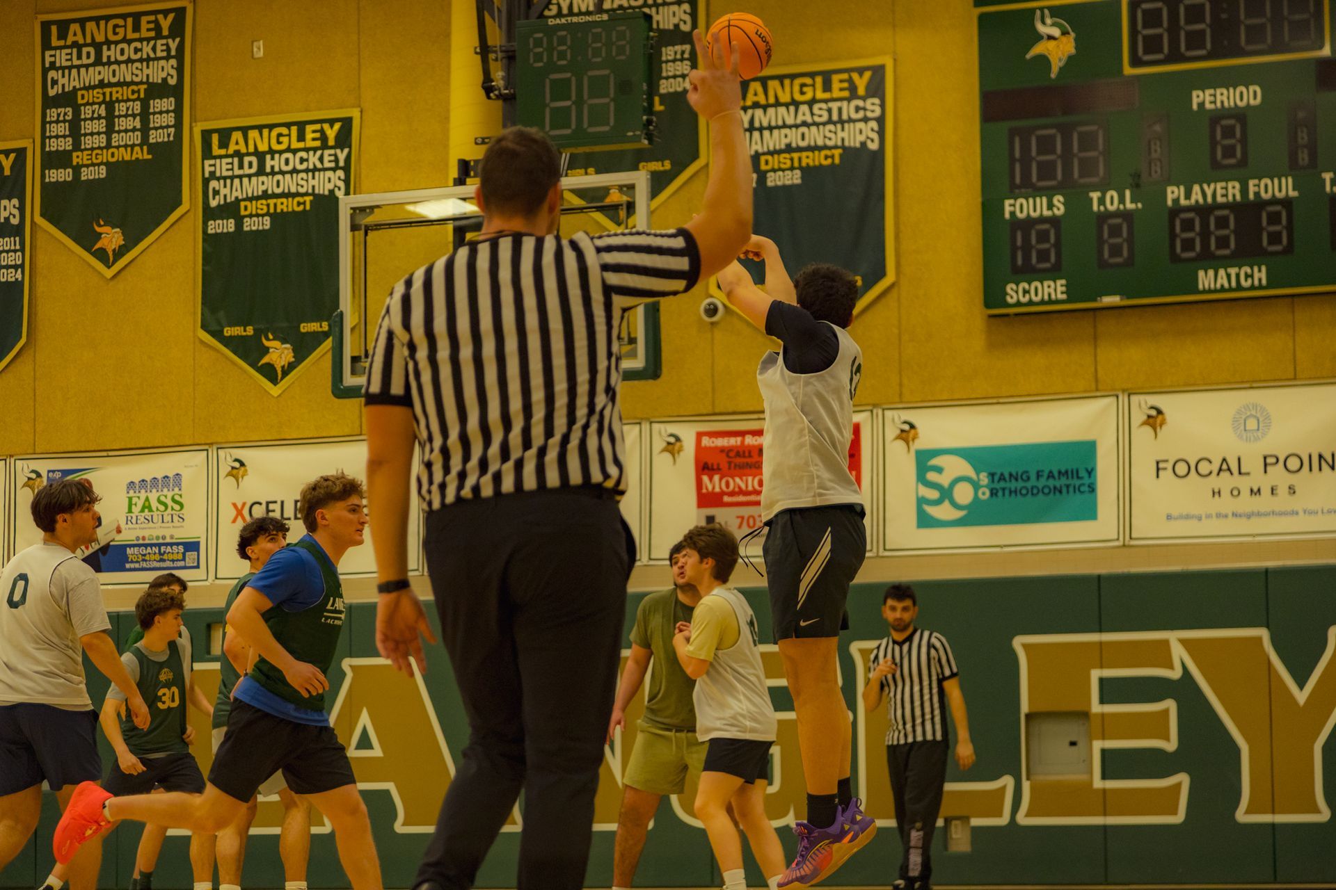 Basketball tipoff at Langley gym, with referee and players jumping for the ball